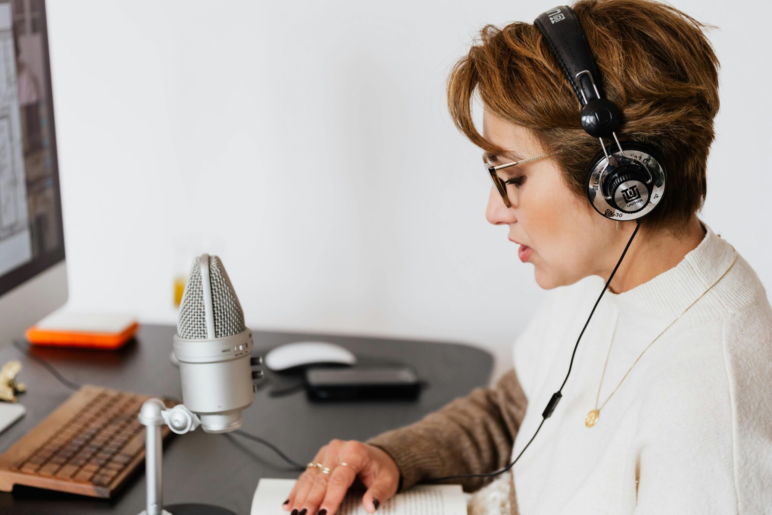 Woman with headphones speaking into a microphone in a modern home studio.